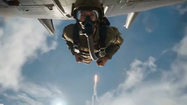 A skydiver in full gear with oxygen mask and goggles captured mid-jump from below, with an aircraft visible above and a missile trail far below against a bright blue sky